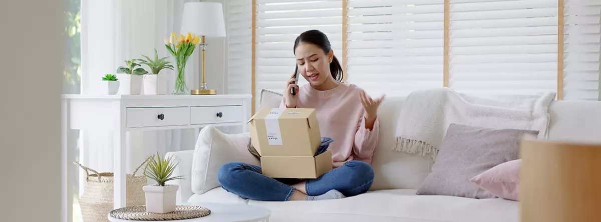 A customer is sitting on her couch and feeling upset because her package has arrived damaged.